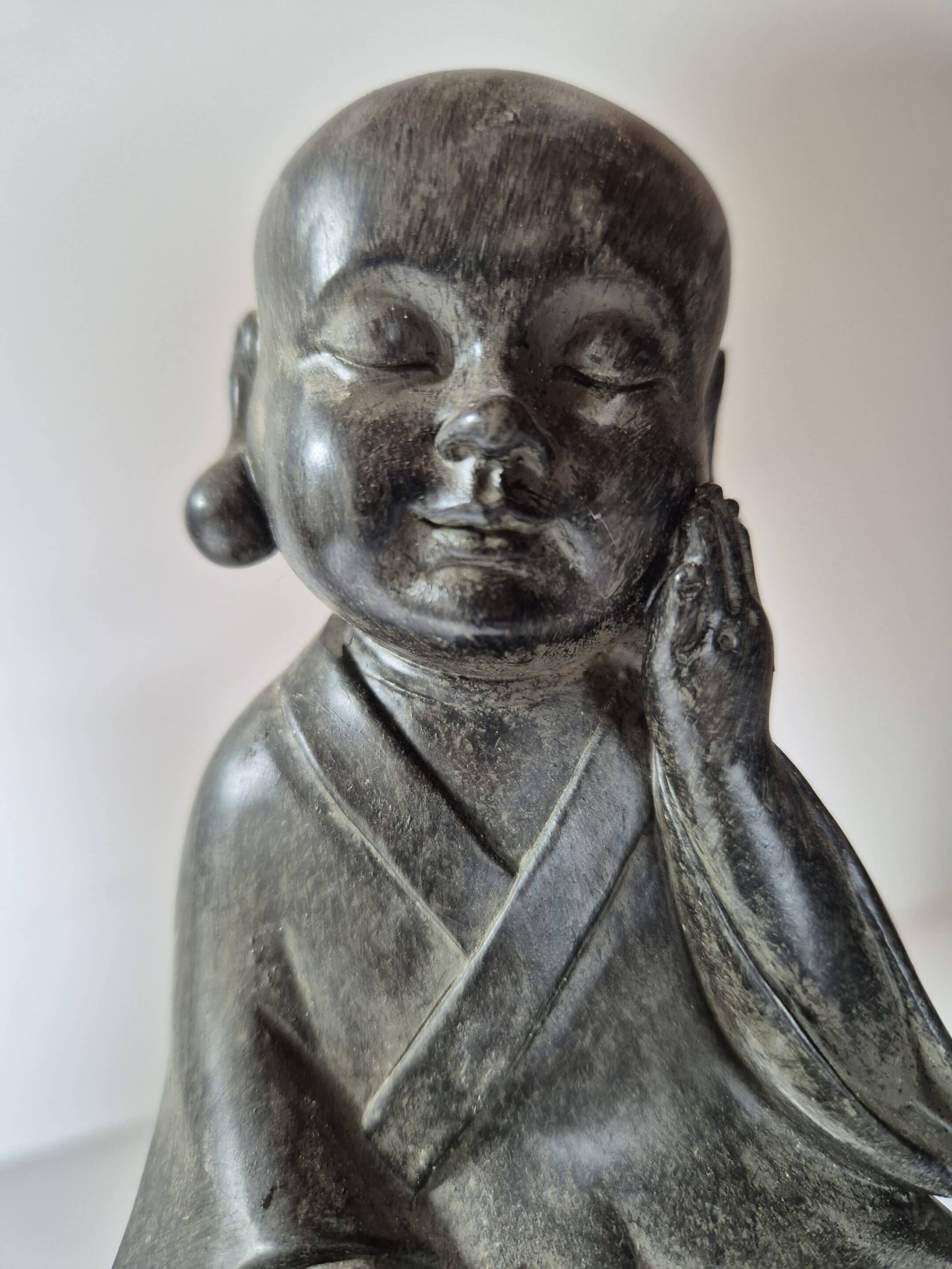 Zoom sur le visage du bouddha. Yeux fermer, main gauche sur la jour et petit sourire. L'oreille droite est apparente avec une grosse boucle d'oreille sphérique.